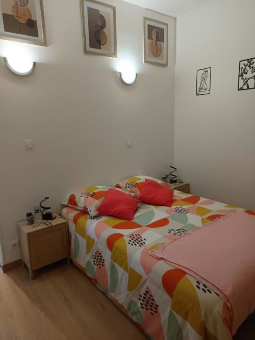 Chambre moderne à Pont-Sainte-Maxence avec literie géométrique colorée, coussins rouges, œuvres murales et appliques