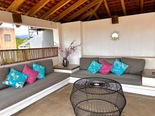Moderna zona de descanso en Casa Tsuki, Puerto Escondido, con asientos grises, cojines coloridos, vigas de madera y vista al océano