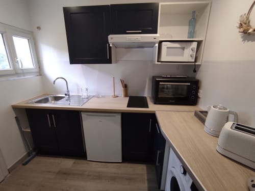 Cuisine compacte du gîte Accolade à Châteaudun avec placards noirs, évier, cuisinière, micro-ondes et électroménagers de comptoir