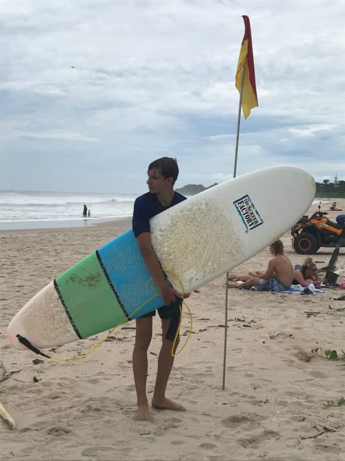 Surfer holding board at Nosara beach with safety flag and waves in background