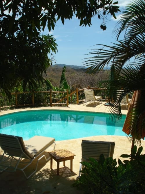 Turquoise pool at Villa Mango B&B in Nosara, Costa Rica, surrounded by palm trees and lounge chairs with mountain views