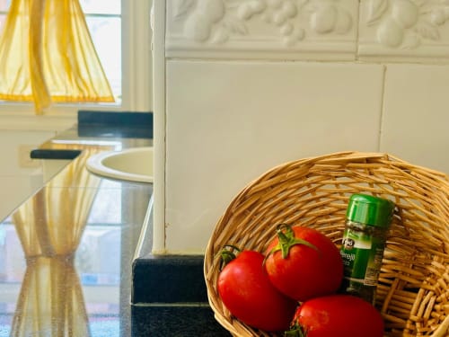 Cesta de mimbre con tomates frescos y botella verde en la cocina del apartamento Holibai, Baiona, España