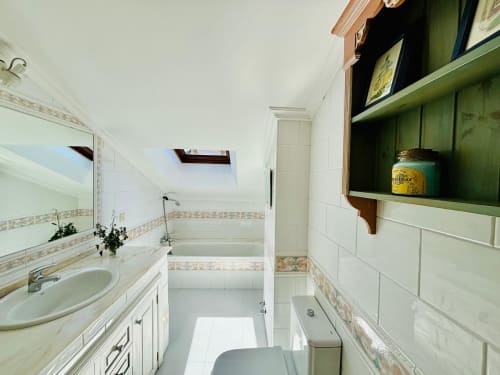 Baño moderno en apartamento dúplex Holibai, Baiona, con azulejos blancos, lavabo, bañera, ducha y estanterías verdes