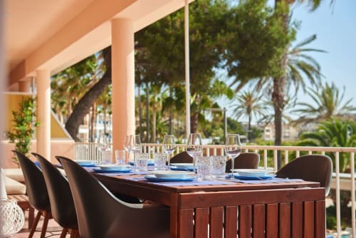 Terrassa de menjador a primera línia de mar a SAND Apartment, Colonia de Sant Jordi, amb taula servida, copes de vi i vistes al mar entre palmeres