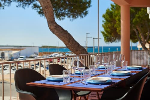 Taula de menjador a primera línia de costa amb copes i relleus blaus amb vistes al Mediterrani a Colònia de Sant Jordi