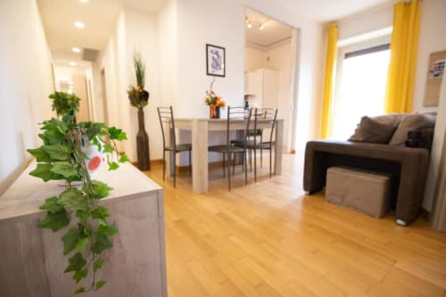 Appartamento Dimore Verona con pavimenti in legno, divano marrone, tavolo da pranzo, tende gialle e piante