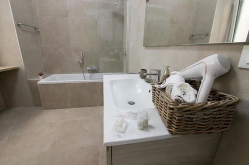 Bagno moderno dell'appartamento Dimore Verona con lavabo bianco, cesto di storage intrecciato e cabina doccia piastrellata