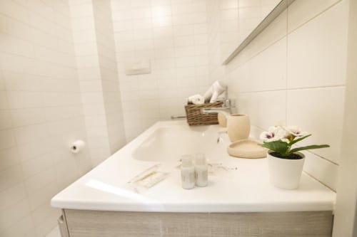 Luminoso vanity del bagno a Dimore Verona con lavabo bianco, orchidea in vaso e amenities in tonalità crema