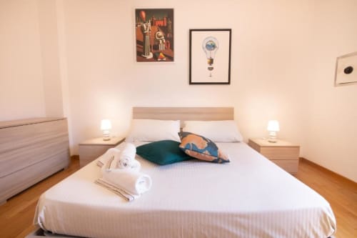 Camera moderna presso l'appartamento Dimore Verona a Verona, con letto bianco, testiera in legno, cuscini decorativi e lampade da comodino