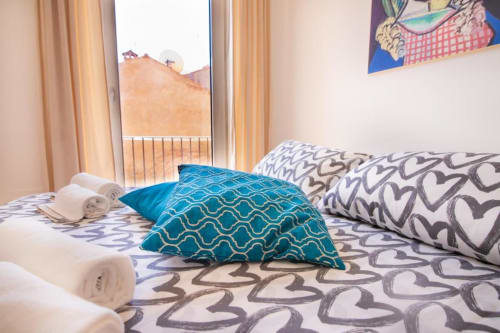 Camera da letto dell'appartamento Bright Dimore Verona con cuscini turchesi decorati, asciugamani arrotolati e vista sulla città dalle finestre