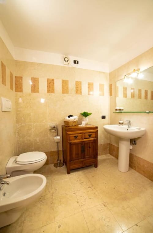 Ampio bagno dell'appartamento Dimore Verona a Verona con piastrelle color crema, mobile in legno, lavabo su colonna, bidet e specchio