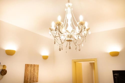 Un elegante lampadario e applique dorate illuminano la camera color crema dell'appartamento Dimore Verona a Verona, Italia