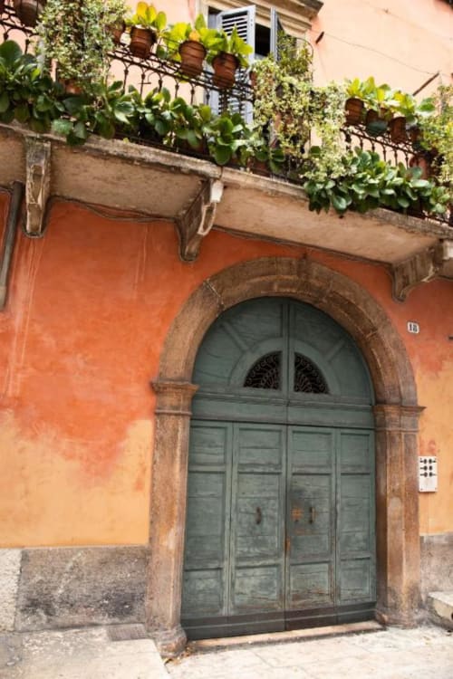 Ingresso storico di palazzo veronese con facciata in terracotta, porta verde e balcone con giardino rigoglioso a Dimore Verona