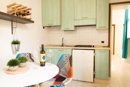 Zona cucina-pranzo moderna nell'appartamento Dimore Verona con mobili verde menta, tavolo rotondo bianco e vista sul giardino