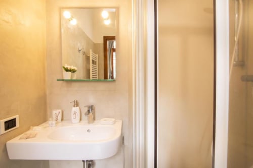 Bagno moderno a Dimore Verona con lavabo bianco curvo, specchio illuminato e box doccia