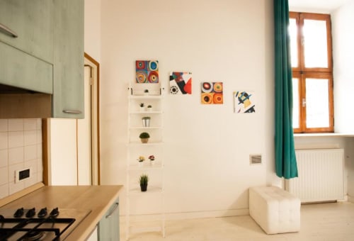 Area cucina-living moderna di Dimore Verona con mobili verde salvia, piani in legno e arte murale colorata