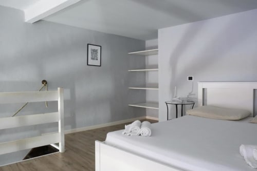 Camera da letto moderna a Dimore Verona con letti bianchi, pareti grigie, mensole sospese e arredamento minimalista a Verona,