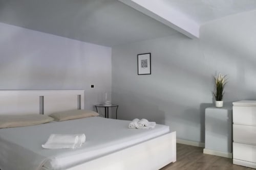 Camera da letto moderna a Dimore Verona con letto bianco, dettagli grigi, pianta in vaso e arredo minimalista nell'appartamento veronese.