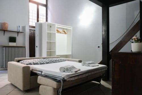 Monolocale moderno a Dimore Verona con divano letto convertibile, armadio bianco e arredi contemporanei