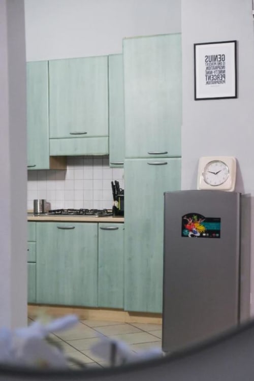 Cucina verde menta con fornello a gas, frigorifero grigio, orologio bianco e quadri all'appartamento Dimore Verona a Verona