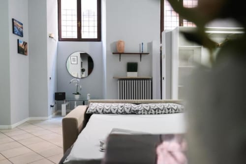 Camera luminosa e moderna a Dimore Verona con specchio rotondo, ripiani in legno, radiatore e biancheria a motivi