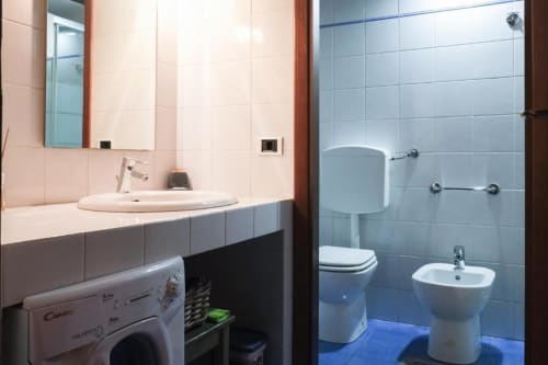 Bagno moderno nell'appartamento Dimore Verona con lavabo rotondo, wc, bidet, lavatrice e piastrelle blu