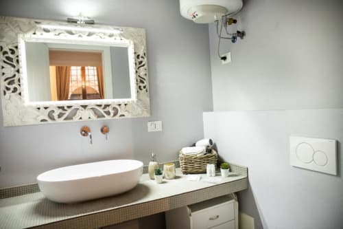 Bagno moderno a Dimore Verona con lavabo ovale bianco, specchio illuminato e accessori decorativi sul ripiano