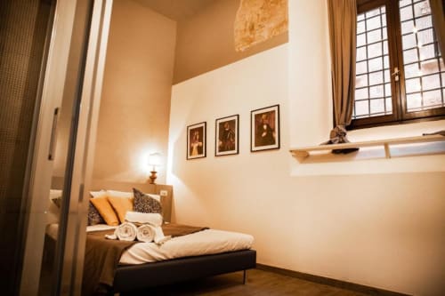 Accogliente camera da letto con illuminazione calda, letto in legno, asciugamani arrotolati, quadri, grande finestra - Dimore Verona