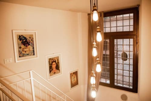 Elegante vano scale presso Dimore Verona con opere d'arte incorniciate, luci pendenti e porta in legno marrone