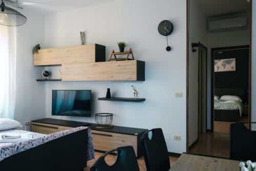 Moderno monolocale a Dimore Verona con mensole in legno, TV, scrivania e vista della camera da letto attraverso la porta.