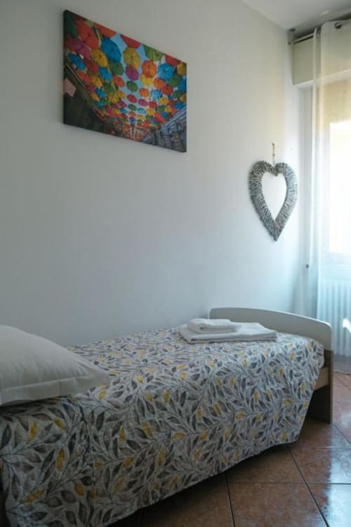 Camera luminosa a Dimore Verona con copriletto a motivi, ombrello colorato come decorazione murale e cuore decorativo