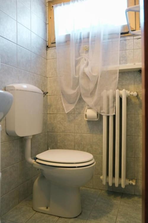 Bagno moderno dell'appartamento Dimore Verona con toilette, tenda doccia, radiatore e pareti piastrellate