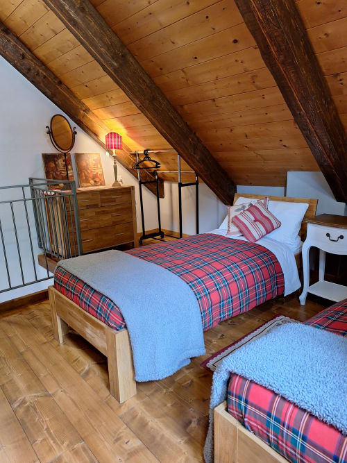 Rustikales Dachzimmmer in der Locanda del Sasso in Crodo mit Holzbalken, karierter Bettwäsche und sichtbarem Holzgebälk