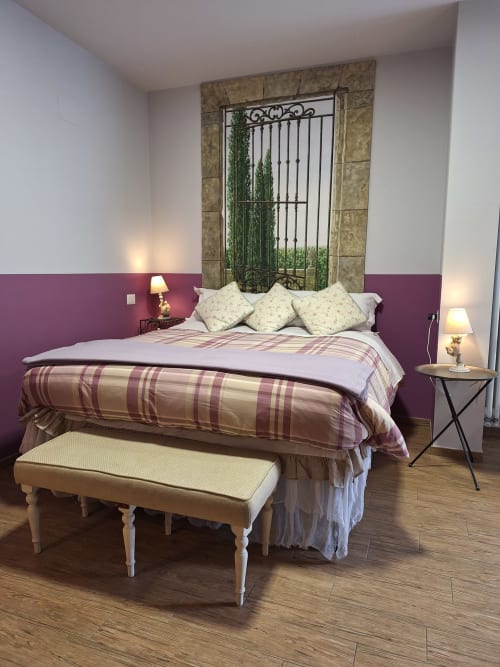 Elegantes Zimmer in der Locanda del Sasso mit lila Akzentwand, karierter Bettwäsche und dekorativem Kunstkopfteil aus Schmiedeeisen in Crodo.