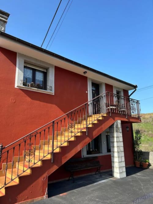 Fachada roja del apartamento Las Llaviadas con escaleras amarillas y vistas a las montañas en Ortiguero de Cabrales