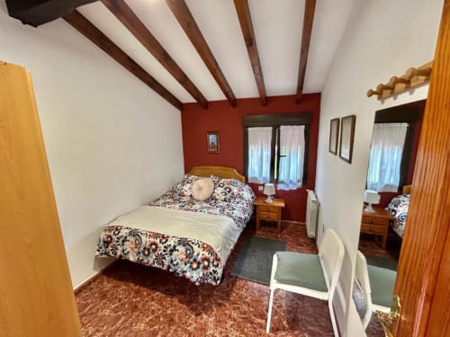 Acogedora habitación del apartamento Las Llaviadas en Ortiguero de Cabrales con vigas vistas, pared acentuada en rojo y vistas a la montaña
