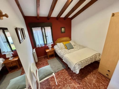 Acogedora habitación de apartamento de montaña en Las Llaviadas, Ortiguero de Cabrales, con vigas vistas, pared de acento rojo y detalles en madera