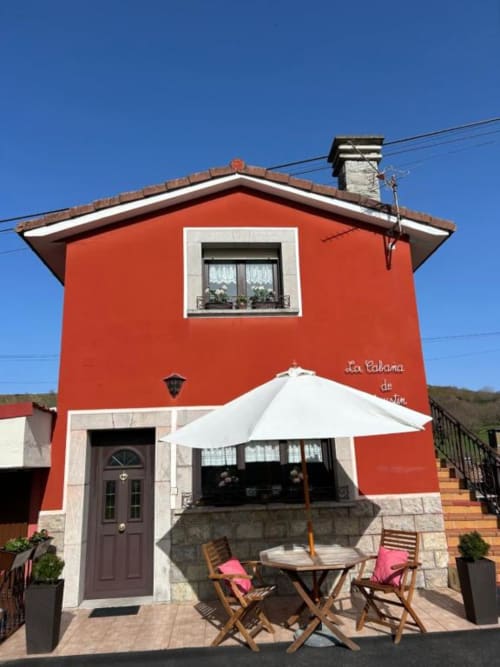 Edificio de apartamentos rojo brillante Las Llaviadas en Ortiguero de Cabrales con sombrilla blanca y zona de estar