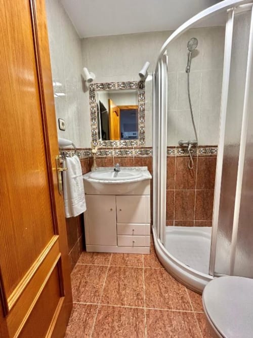 Baño moderno en apartamento Las Llaviadas de Ortiguero de Cabrales con ducha curva, lavamanos esquinero y baldosas de barro