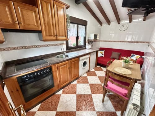Cocina-salón del apartamento Las Llaviadas con muebles de madera, sofá rojo y suelo de baldosas a cuadros en Cabrales