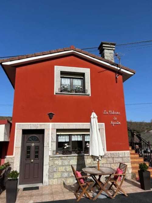 Fachada roja vibrante en Las Llaviadas, Ortiguero de Cabrales, con vistas a las montañas, terraza y detalles en blanco