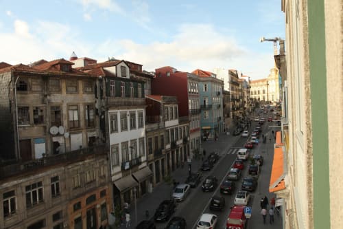 Vista da rua do Porto com edifícios históricos coloridos, carros estacionados e céu azul - localização do New Oporto Apartments