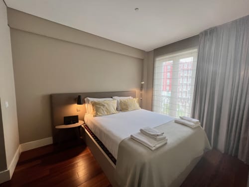 Quarto moderno no New Oporto Apartments no Porto com cama queen, paredes bege, piso de madeira escura e vista para a cidade do balcão