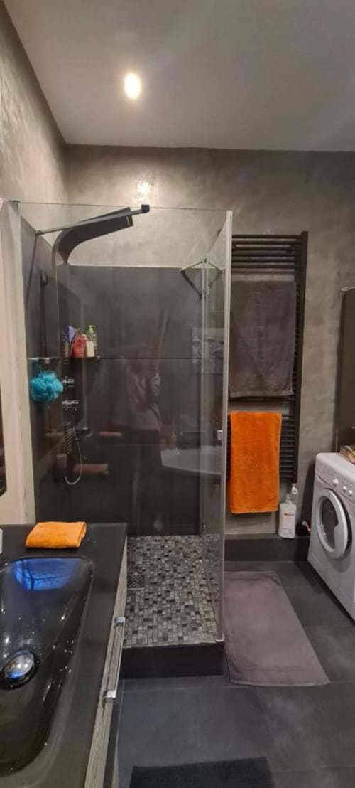 Salle de bains moderne du Cocon de Chris Marseille avec douche vitrée, carrelage foncé, serviettes oranges et lave-linge