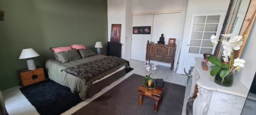 Chambre de Le Cocon de Chris à Marseille avec murs verts, mobilier en bois et orchidées blanches sur la commode