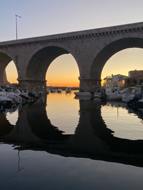 Arches en pierre surplombant le port tranquille au coucher de soleil à Marseille, bateaux amarrés à proximité