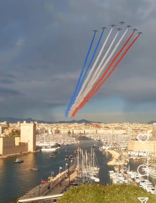 Des avions militaires français effectuant une démonstration aérienne avec fumée bleu, blanc et rouge au-dessus du port de Marseille et des voiliers