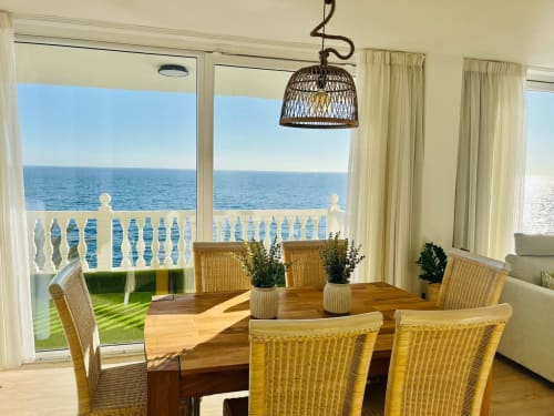 Coastal dining room with ocean view, woven pendant lamp, wooden table, rattan chairs, and terrace overlooking Arguineguín