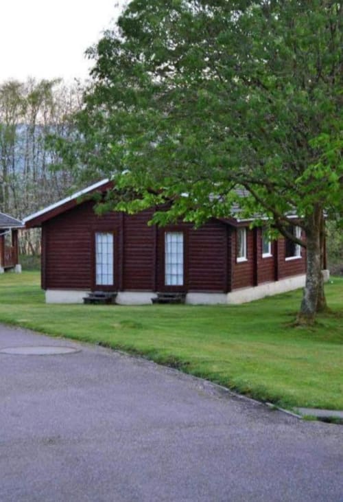 Dark wood lodge cabin at Grouse Lodge in Dunoon surrounded by green lawn and large trees