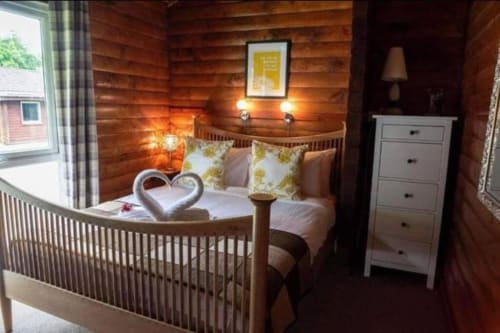 Cozy log cabin bedroom at Grouse Lodge, Dunoon with double bed, white dresser, and warm lighting